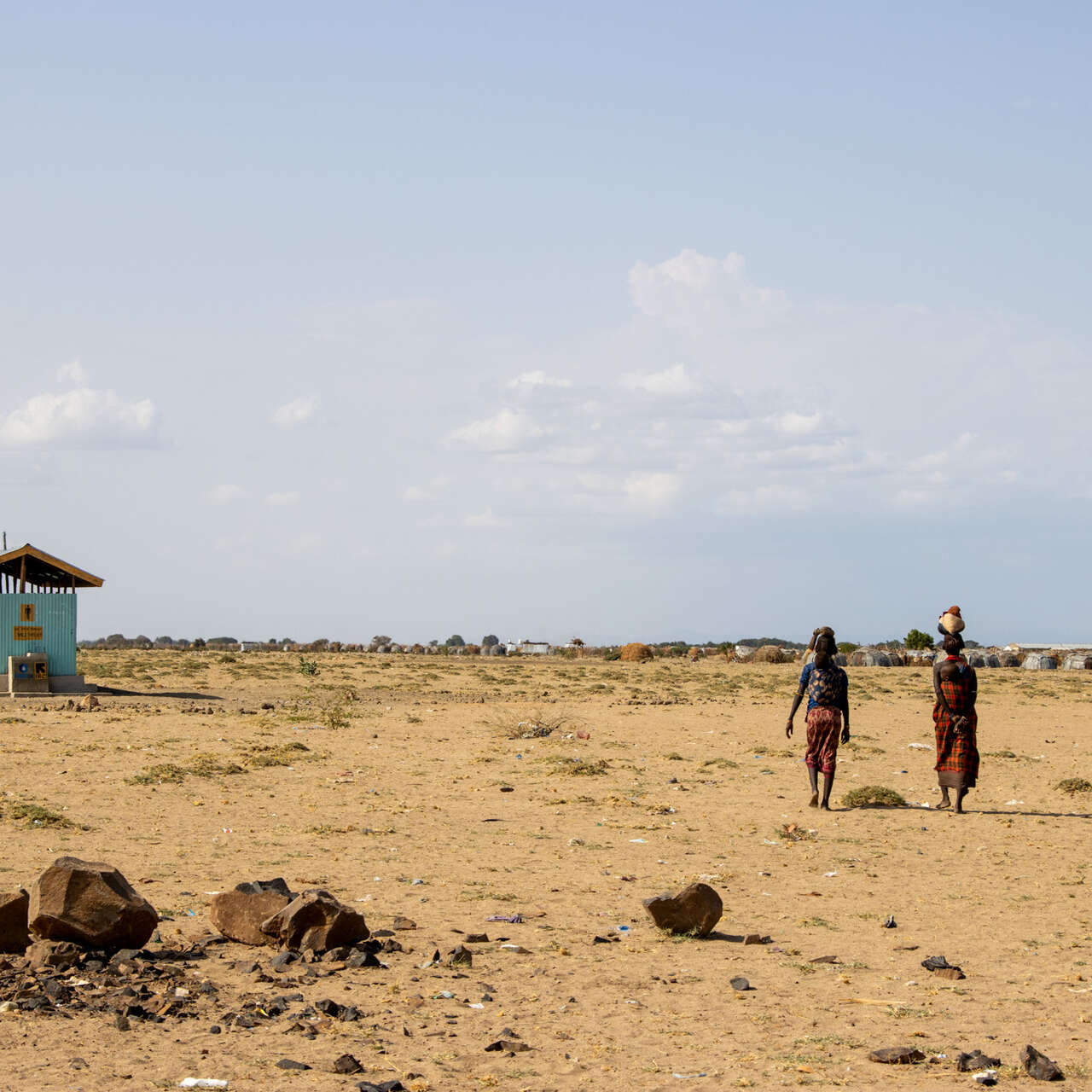 Two women walk away from the camera. In the background lies a barren Ethiopia landscape, dotted by an IRC-supported water facility.